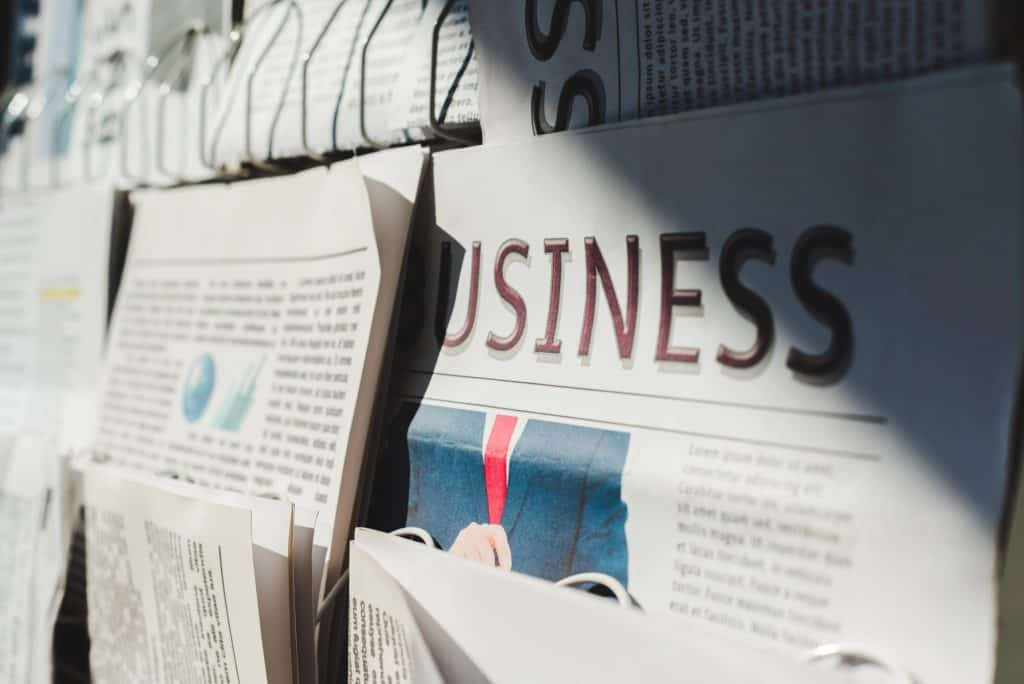 A rack of newspapers with the large heading "Business," partially obscured by shadows.