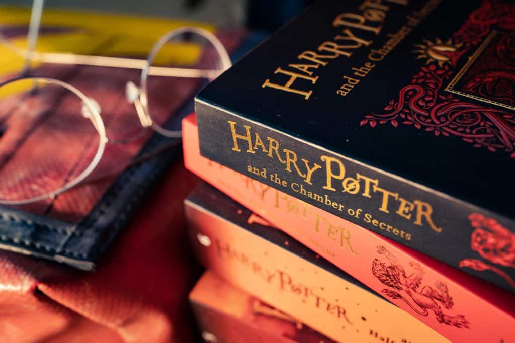 A close-up of stacked "Harry Potter" books with glasses resting on a red fabric in the background.