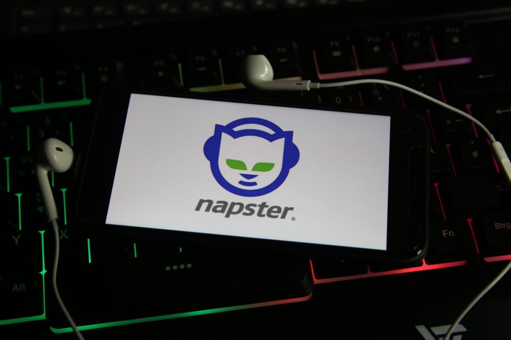 A smartphone displaying the Napster logo with earbuds placed on top of a backlit keyboard.