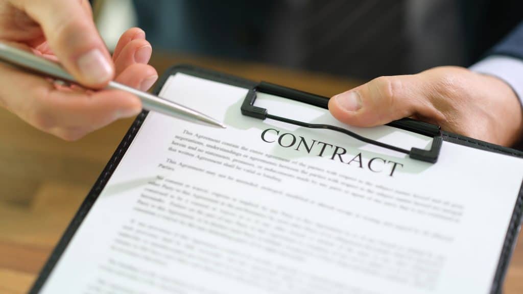 A close-up of a person holding a pen over a clipboard with a contract document titled "Contract."