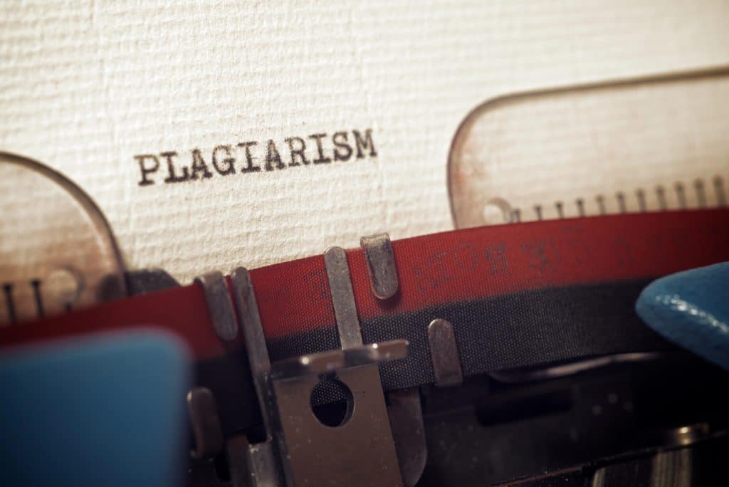 The word "plagiarism" typed on paper using a vintage typewriter with a red and black ribbon.