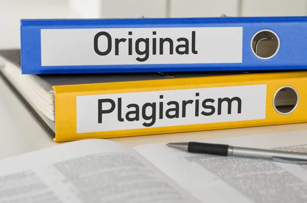 Two labeled binders, one blue with "Original" and one yellow with "Plagiarism," placed on a desk with an open book and pen.