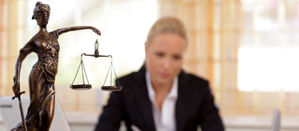 An image focused on statue holding a beam scale with a blurred-out lawyer sitting on a background.