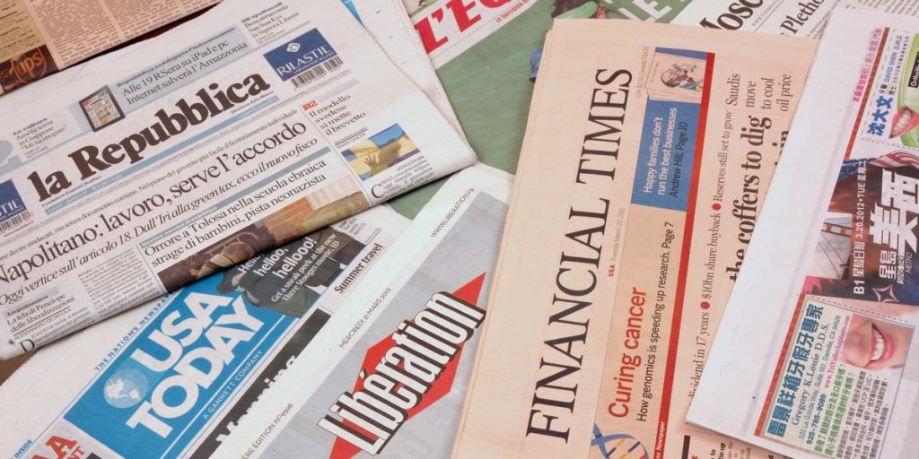 A close-up of a pile of newspapers with different headlines are shown.