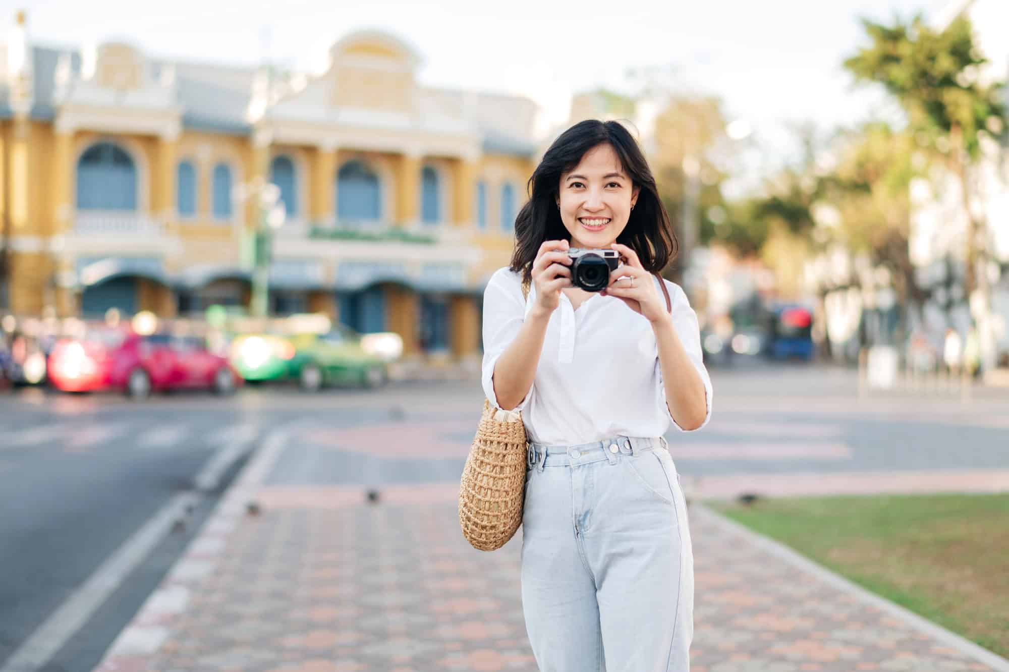 A woman in white a white blouse smiling while holding a camera.