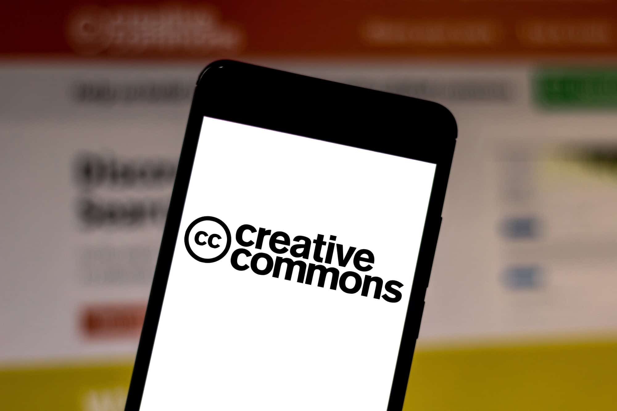 A smartphone displaying the "Creative Commons" logo on a white screen, with a blurred background of a webpage.